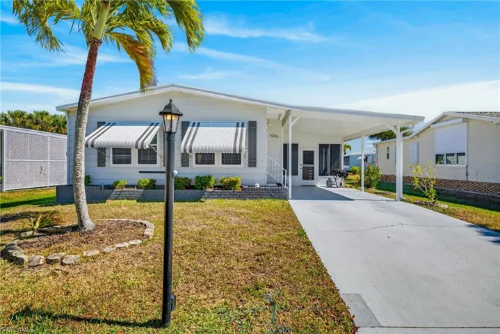 Manufactured / mobile home with a front lawn, a carport, concrete driveway, and a porch