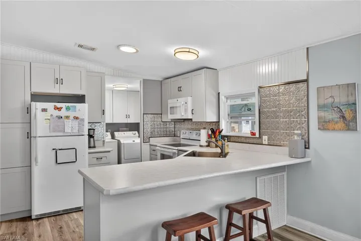Kitchen featuring white appliances, light countertops, light wood-type flooring, a peninsula, and a kitchen bar
