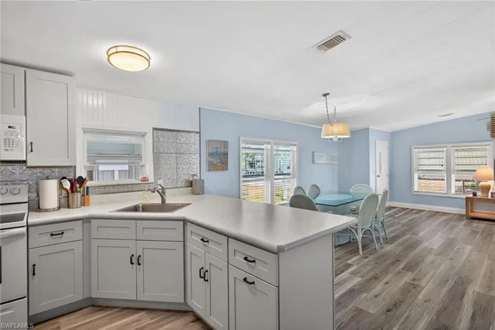 Kitchen featuring white appliances, a peninsula, light wood finished floors, and light countertops