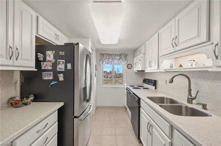 Kitchen with stainless steel fridge with ice dispenser, white cabinetry, light tile patterned floors, and white microwave