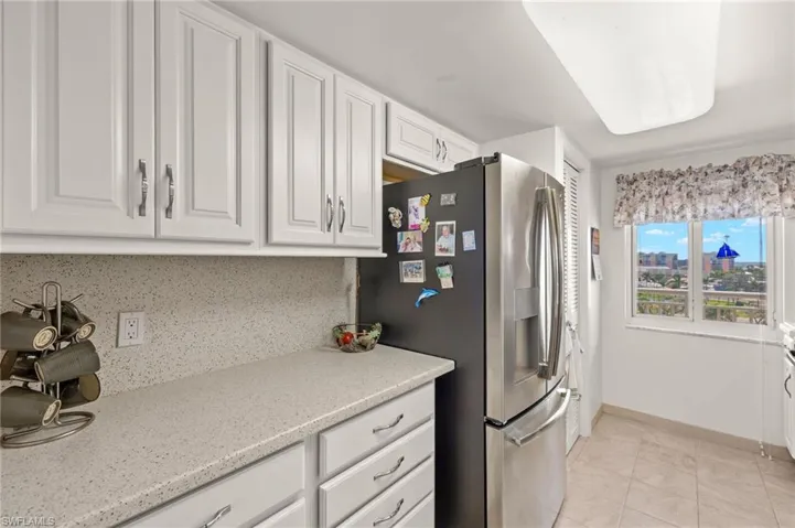 Kitchen with stainless steel refrigerator with ice dispenser, white cabinets, light tile patterned flooring, and light stone countertops