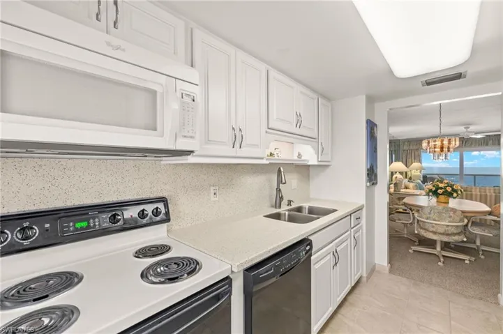 Kitchen with white microwave, range with electric cooktop, dishwasher, a chandelier, and white cabinets