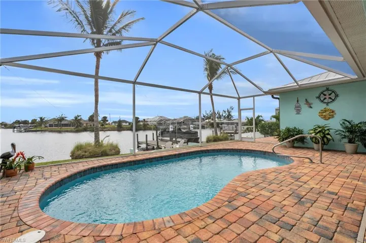 Outdoor pool with boat lift, a dock, a water view, glass enclosure, and a patio area
