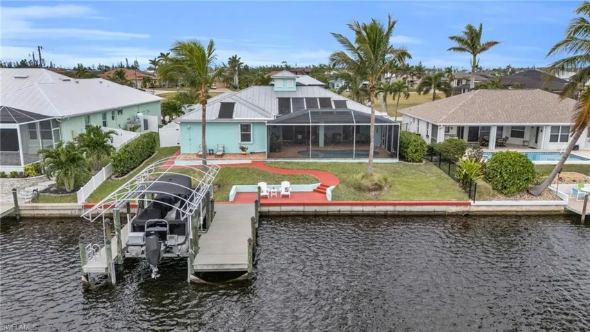 Dock area featuring boat lift, a fenced backyard, a water view, glass enclosure, and a yard