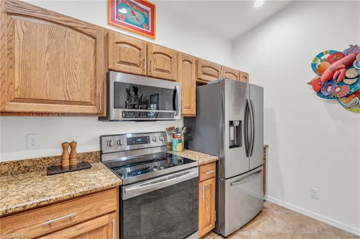Kitchen featuring baseboards, stainless steel appliances, light tile patterned flooring, and light stone counters