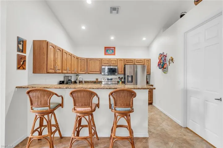 Kitchen featuring stainless steel appliances, a breakfast bar, a peninsula, visible vents, and light stone countertops