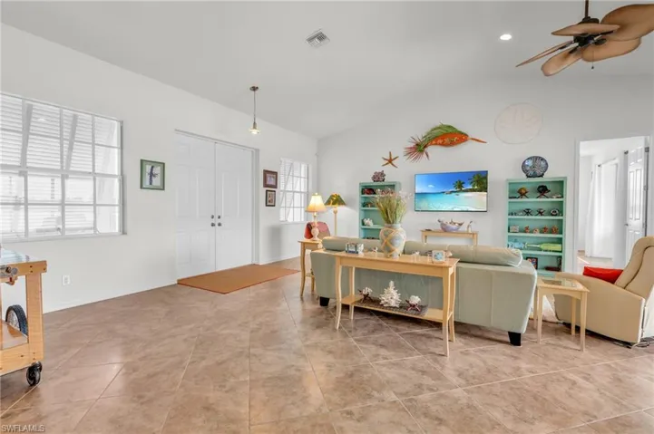 Living area featuring vaulted ceiling, light tile patterned floors, baseboards, ceiling fan, and visible vents
