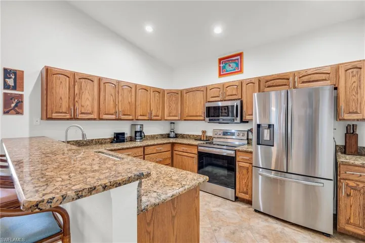 Kitchen featuring a kitchen bar, stainless steel appliances, light stone countertops, a peninsula, and brown cabinets