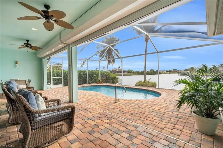 View of pool with a water view, a lanai, ceiling fan, and a patio