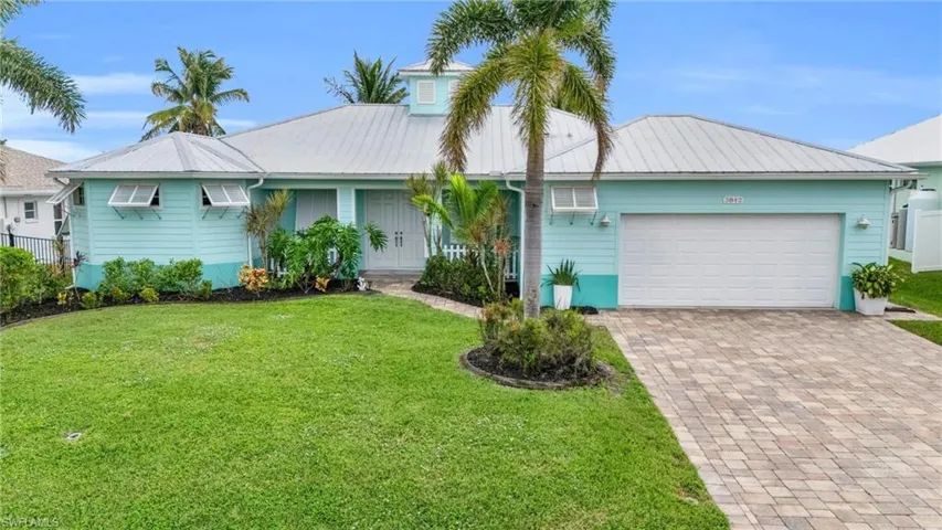 Ranch-style home with a front yard, decorative driveway, an attached garage, and metal roof