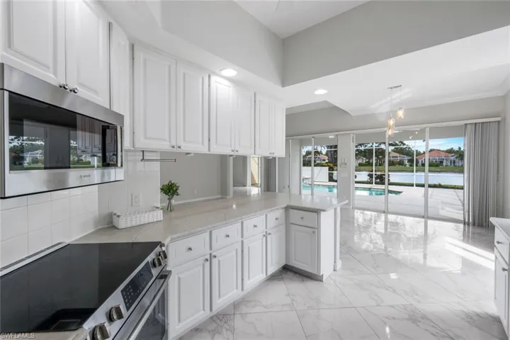 Kitchen with appliances with stainless steel finishes, white cabinetry, light stone counters, light marble finish flooring, and a water view