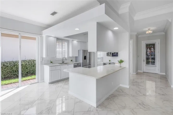 Kitchen with crown molding, light marble finish flooring, a peninsula, light stone countertops, and white cabinets