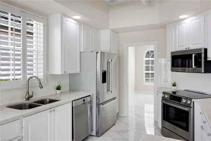 Kitchen featuring backsplash, stainless steel appliances, white cabinetry, light stone countertops, and recessed lighting