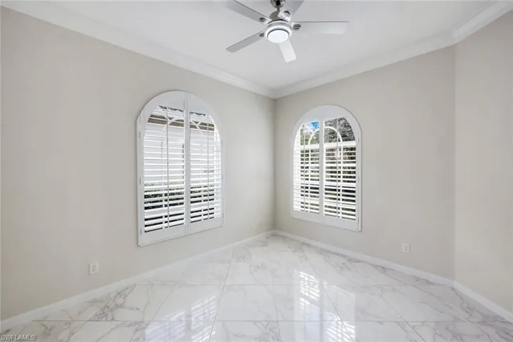 Spare room with light marble finish floors, crown molding, and ceiling fan