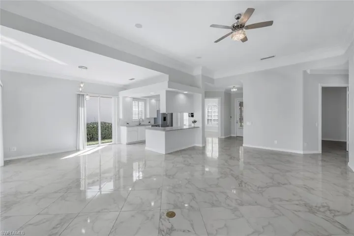 Unfurnished living room featuring crown molding, light marble finish flooring, and ceiling fan