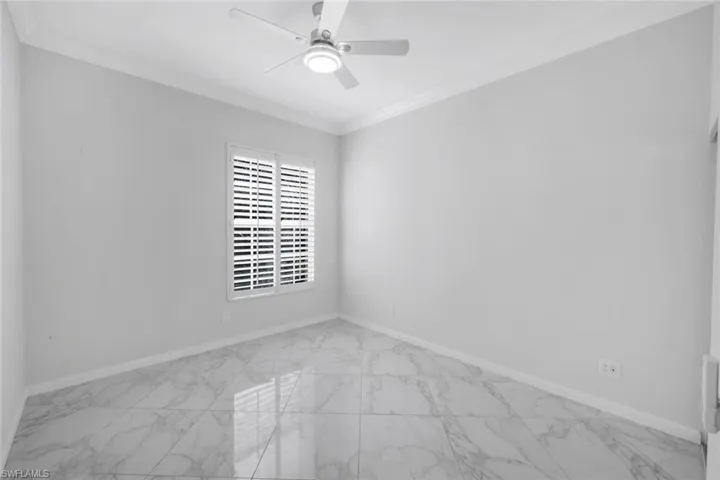 Unfurnished room with light marble finish flooring, ornamental molding, and a ceiling fan