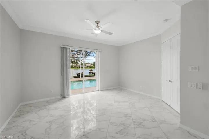 Empty room with light marble finish floors, crown molding, a water view, and a ceiling fan