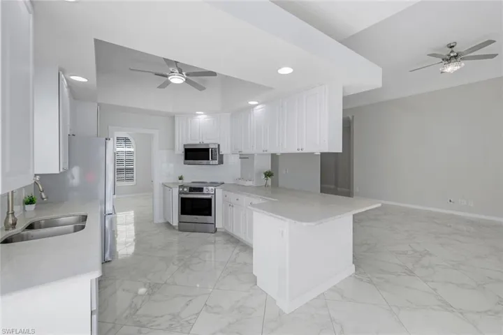 Kitchen featuring a ceiling fan, light marble finish flooring, stainless steel appliances, white cabinetry, and recessed lighting