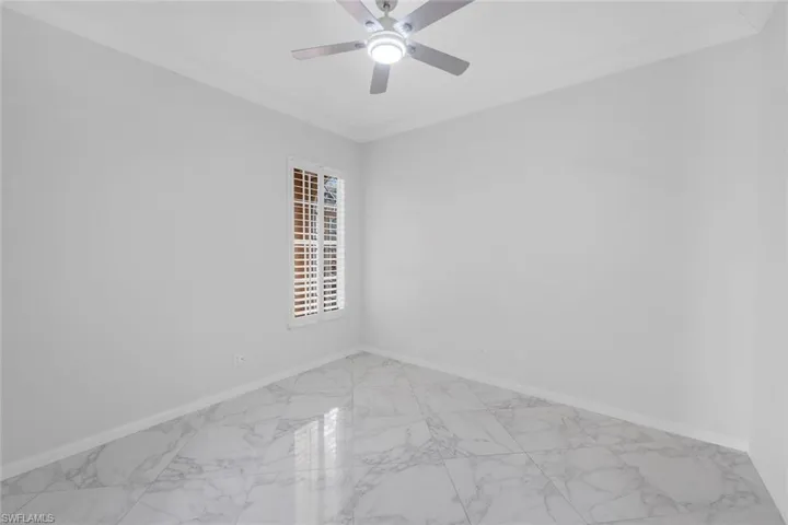 Spare room featuring light marble finish flooring, ornamental molding, and a ceiling fan