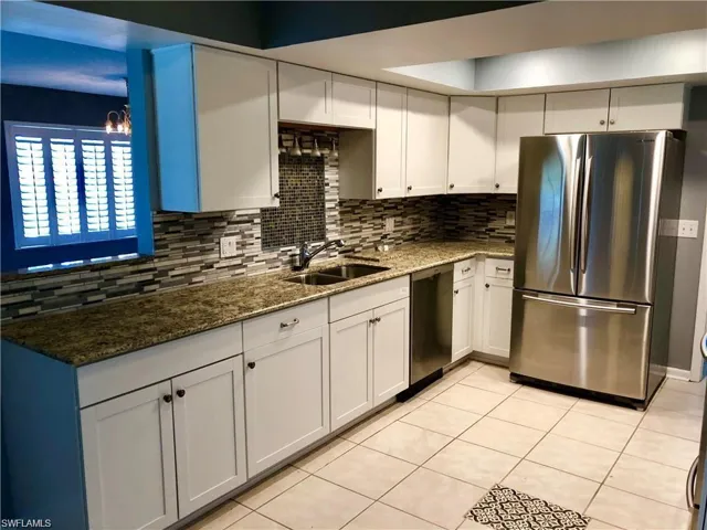 Kitchen featuring dark stone counters, stainless steel appliances, sink, light tile patterned floors, and white cabinetry