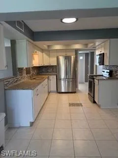 Kitchen featuring decorative backsplash, stainless steel refrigerator, range, white cabinets, and light tile patterned floors