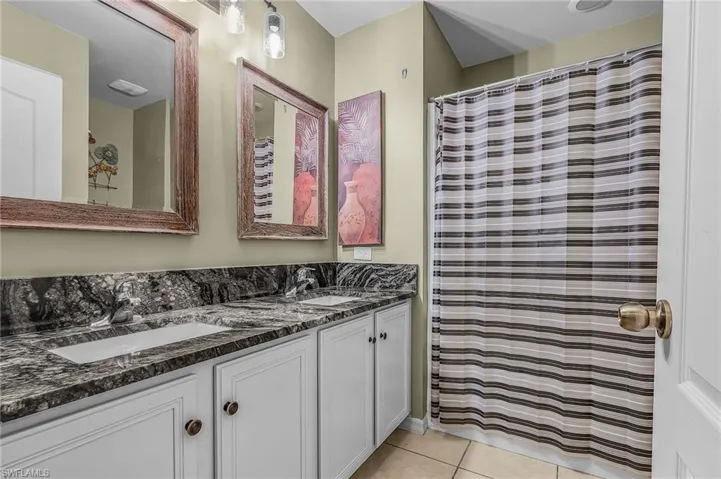 Bathroom with a shower with shower curtain, double vanity, and light tile patterned flooring