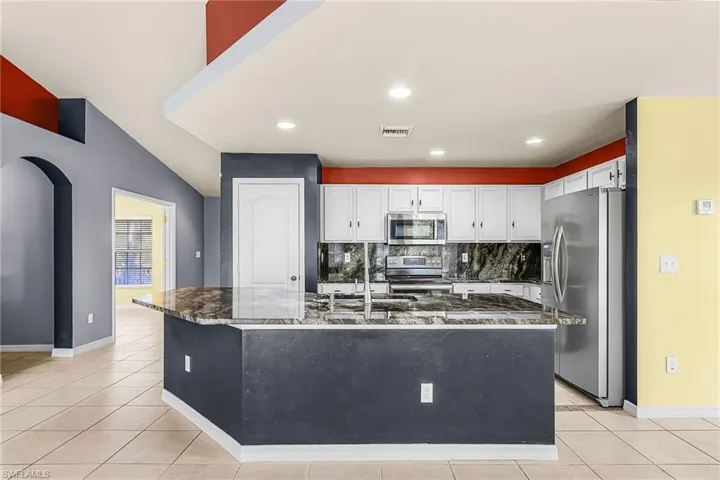 Kitchen with stainless steel appliances, tasteful backsplash, white cabinetry, dark stone countertops, and a center island with sink