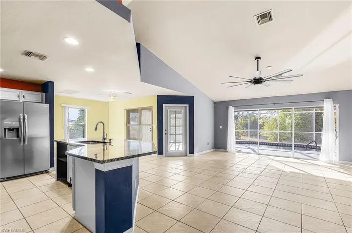 Kitchen with stainless steel refrigerator with ice dispenser, open floor plan, dark stone counters, a kitchen island with sink, and light tile patterned floors