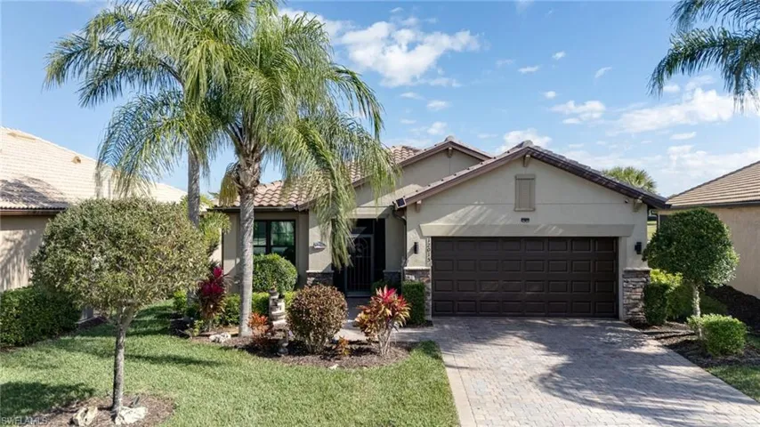 View of front of home featuring stucco siding, decorative driveway, a front lawn, and stone siding