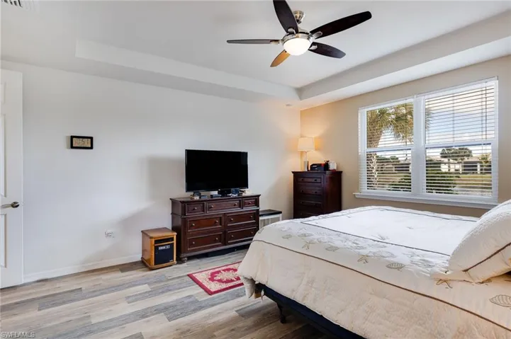Bedroom with a tray ceiling, light wood-type flooring, and a ceiling fan