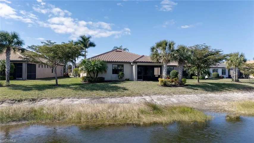 Back of house featuring a water view, a tiled roof, a sunroom, stucco siding, and a yard
