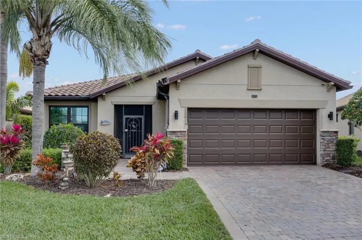 Single story home with stucco siding, stone siding, decorative driveway, a front lawn, and a tile roof