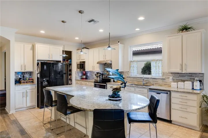 Kitchen featuring a kitchen bar, appliances with stainless steel finishes, crown molding, light stone countertops, and a kitchen island