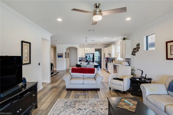 Living area with arched walkways, a ceiling fan, crown molding, light wood-style floors, and recessed lighting