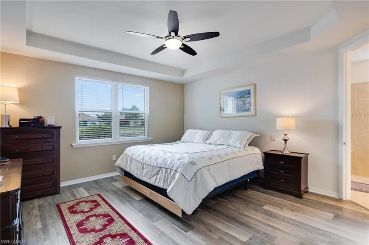 Bedroom featuring a tray ceiling, ceiling fan, wood finished floors, and ensuite bath
