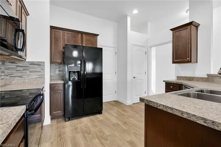 Kitchen with black appliances, light wood-style floors, tasteful backsplash, dark brown cabinetry, and recessed lighting