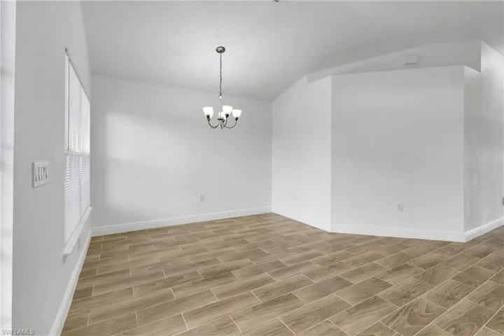 Spare room with vaulted ceiling, wood finish floors, and a chandelier