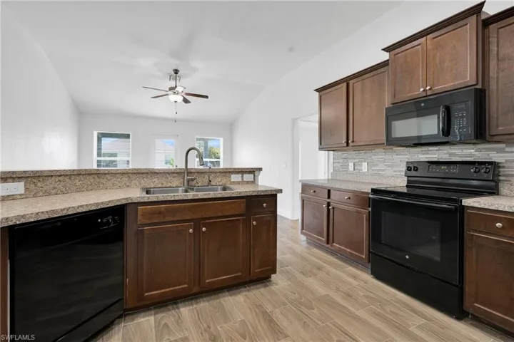 Kitchen with black appliances, a ceiling fan, vaulted ceiling, decorative backsplash, and light countertops