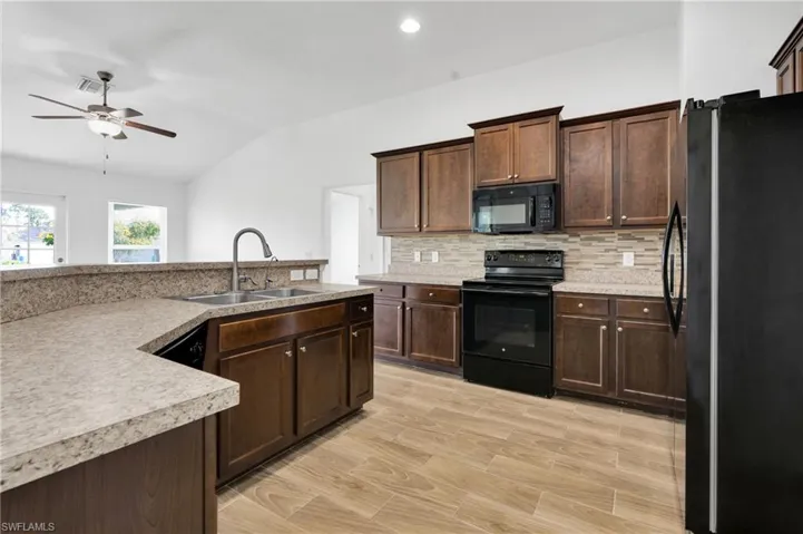 Kitchen with black appliances, ceiling fan, lofted ceiling, decorative backsplash, and light countertops