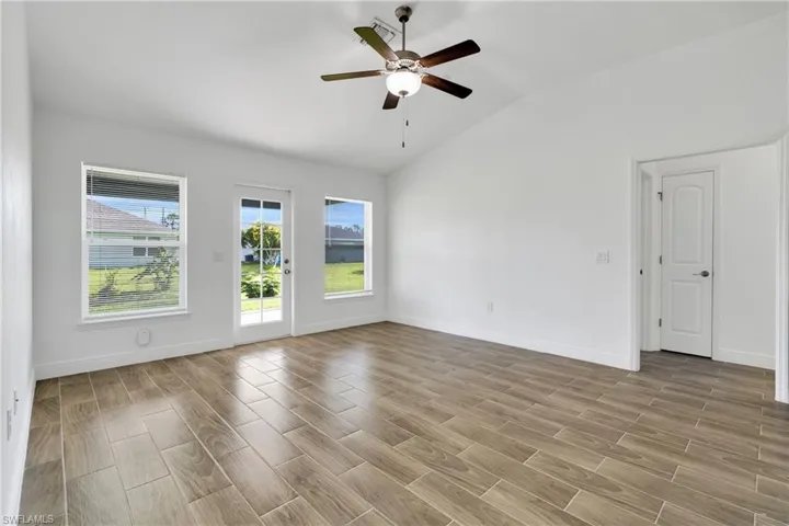 Empty room with lofted ceiling, ceiling fan, and light wood-style flooring