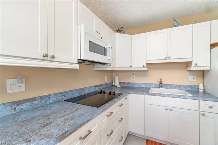 Kitchen featuring sink, black electric cooktop, a textured ceiling, and white cabinets