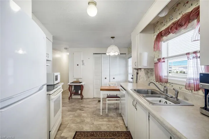 Kitchen featuring white appliances, white cabinetry, light countertops, and hanging light fixtures