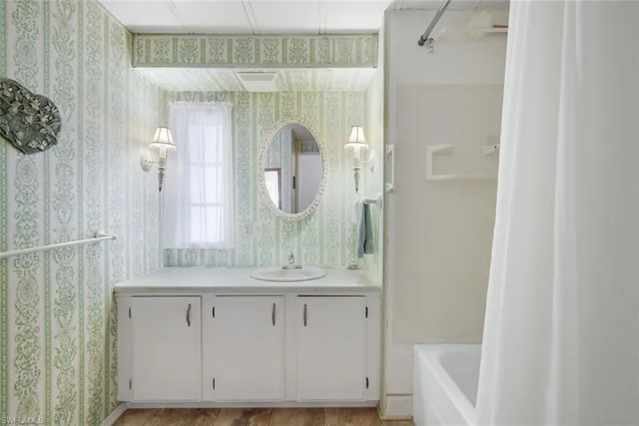 Full bathroom featuring vanity, shower / bath combo, and wallpapered walls