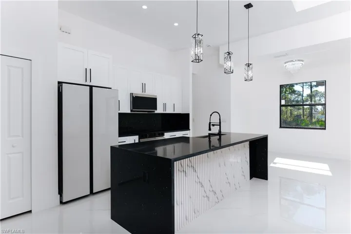 Kitchen with sink, white refrigerator, a center island with sink, a notable chandelier, and white cabinets