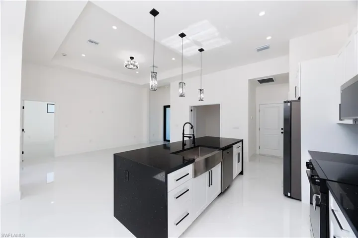 Kitchen with white cabinets, appliances with stainless steel finishes, a tray ceiling, and hanging light fixtures