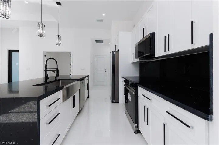 Kitchen featuring appliances with stainless steel finishes, white cabinetry, hanging light fixtures, and an island with sink