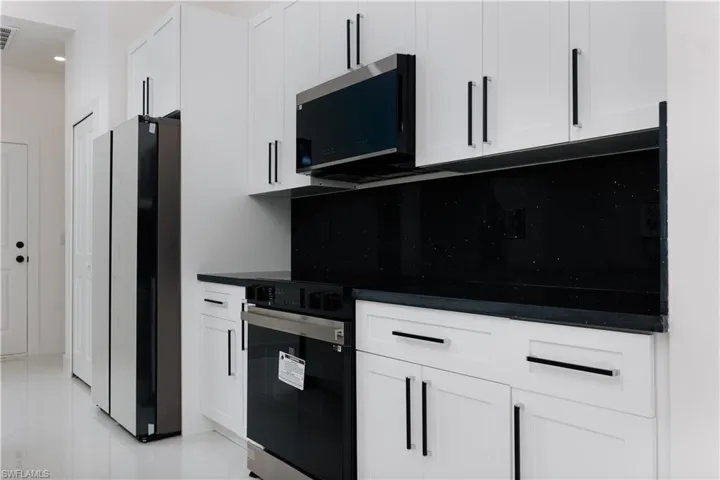 Kitchen featuring decorative backsplash, light tile patterned floors, white cabinetry, and appliances with stainless steel finishes