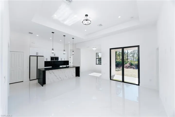 Kitchen featuring stone counters, white fridge, decorative light fixtures, a tray ceiling, and white cabinets