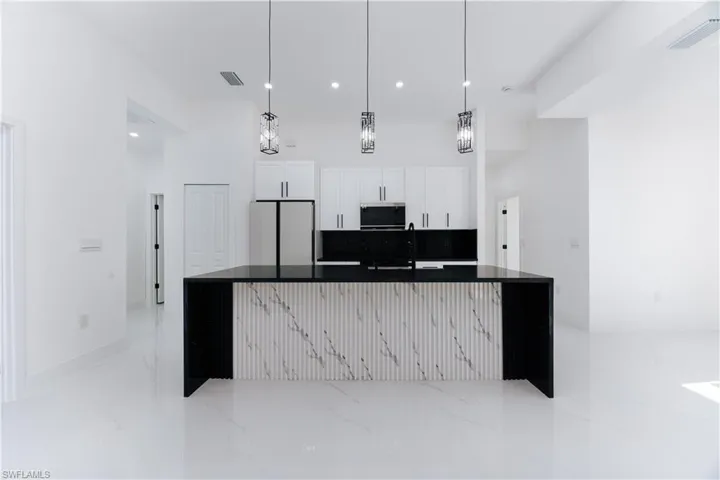 Kitchen with a kitchen island with sink, sink, white cabinets, white fridge, and hanging light fixtures