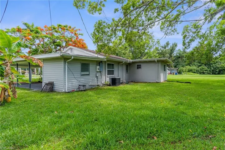 Rear view of house with central AC unit and a lawn